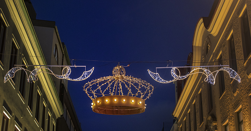 En ljuskrona i centrum av en julljusslinga och av bilden av skymmande himmel över stadsgata