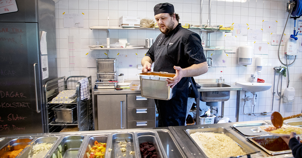 Kock i skolkök som lägger upp mat.